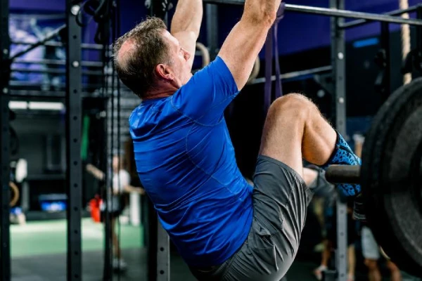 Mature man hanging from a bar and bending his knees over a bar in the gym
