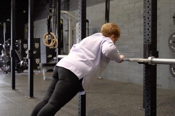 Old lady doing standing barbel pushups